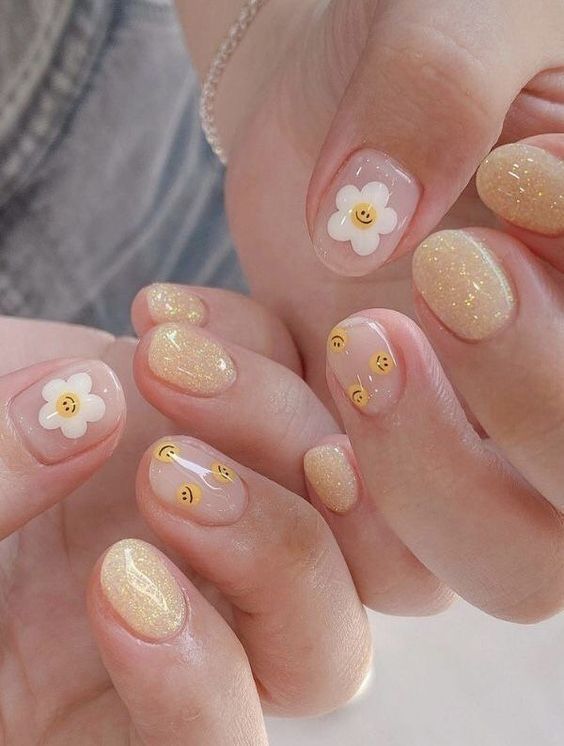 Couleur d’ongle jaune pâle scintillante avec des fleurs blanches et des smileys jaunes sur des ongles ronds courts