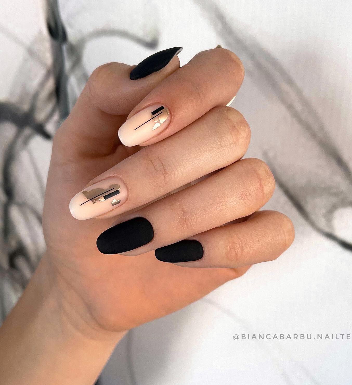 Couleurs d’ongles noires et nude au fini mat avec un nail art élégant en feuille d’or sur des ongles ronds moyens