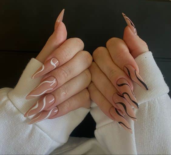 Couleur d’ongle nude au fini brillant avec des tourbillons noirs et blancs sur de longs ongles à talons aiguilles