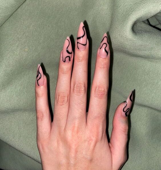 Vernis à ongles nude au fini brillant avec des tourbillons noirs sur de longs ongles à talons aiguilles