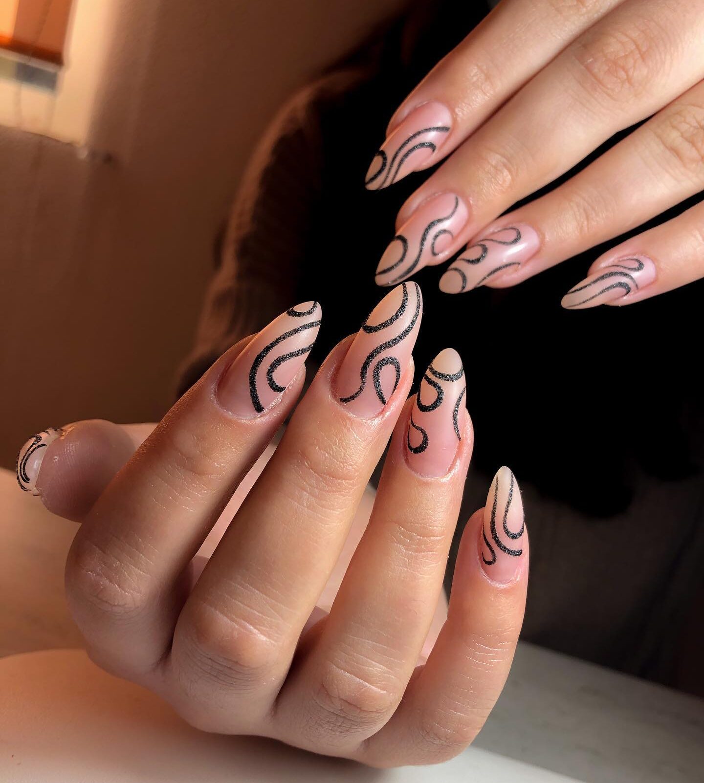 Vernis à ongles nude avec des tourbillons noirs complexes sur de longs ongles en amande