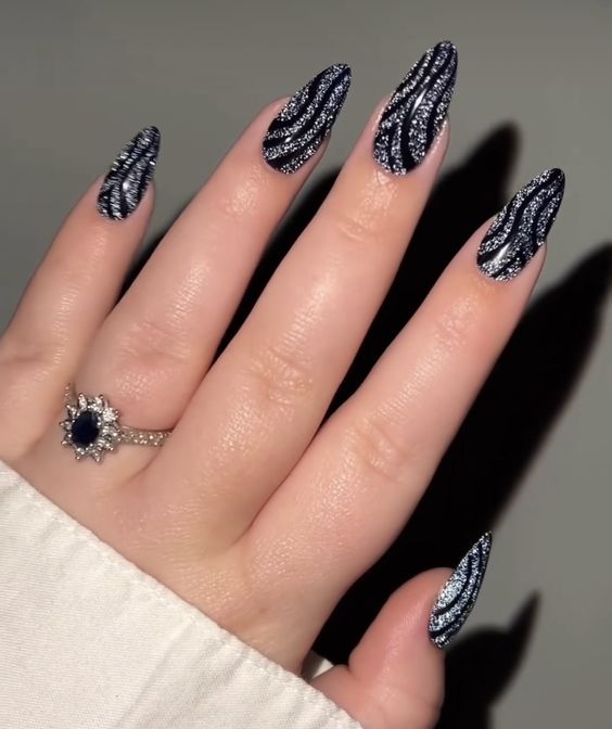 Couleur d’ongle noire avec des tourbillons argentés nail art sur de longs ongles en amande