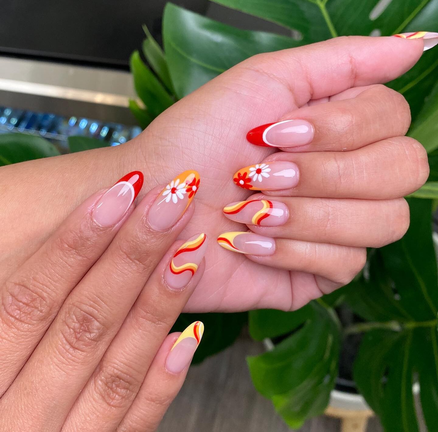 Longs ongles ronds en acrylique transparent avec des pointes françaises rouges et oranges, des tourbillons et des motifs d’ongles floraux