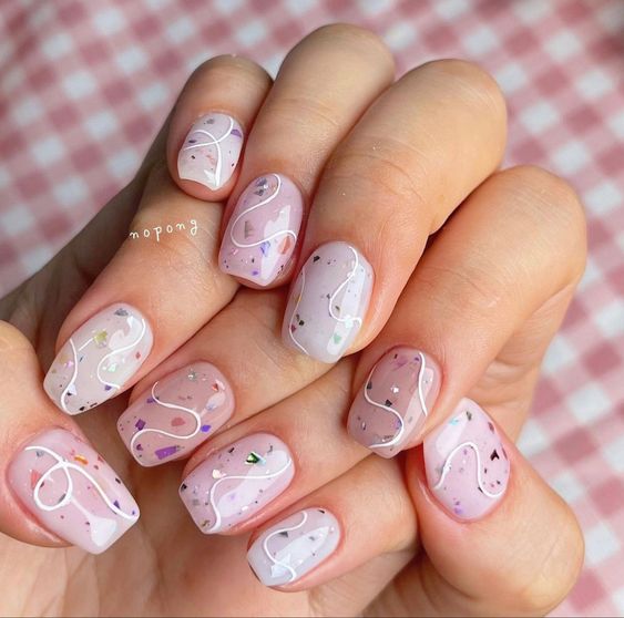 Vernis à ongles de couleur pastel en finition brillante avec des tourbillons blancs et des paillettes sur des ongles de cercueil courts