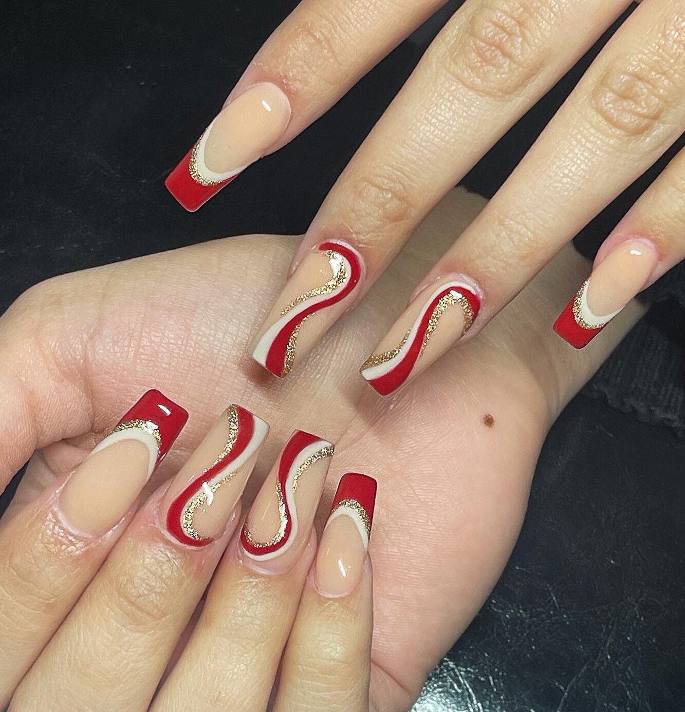 Des pointes françaises rouges, blanches et dorées et des tourbillons de nail art sur de longs ongles de cercueil