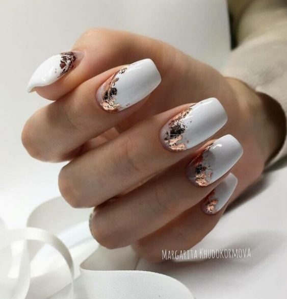 Vernis à ongles de couleur blanche avec des motifs d’ongles en feuille d’or rose sur des ongles carrés effilés moyens