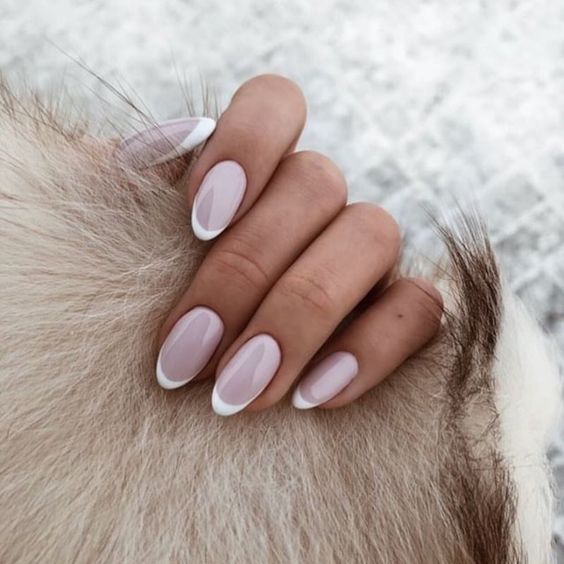 Vernis à ongles blanc pâle avec de fines pointes françaises blanches sur des ongles courts et ronds