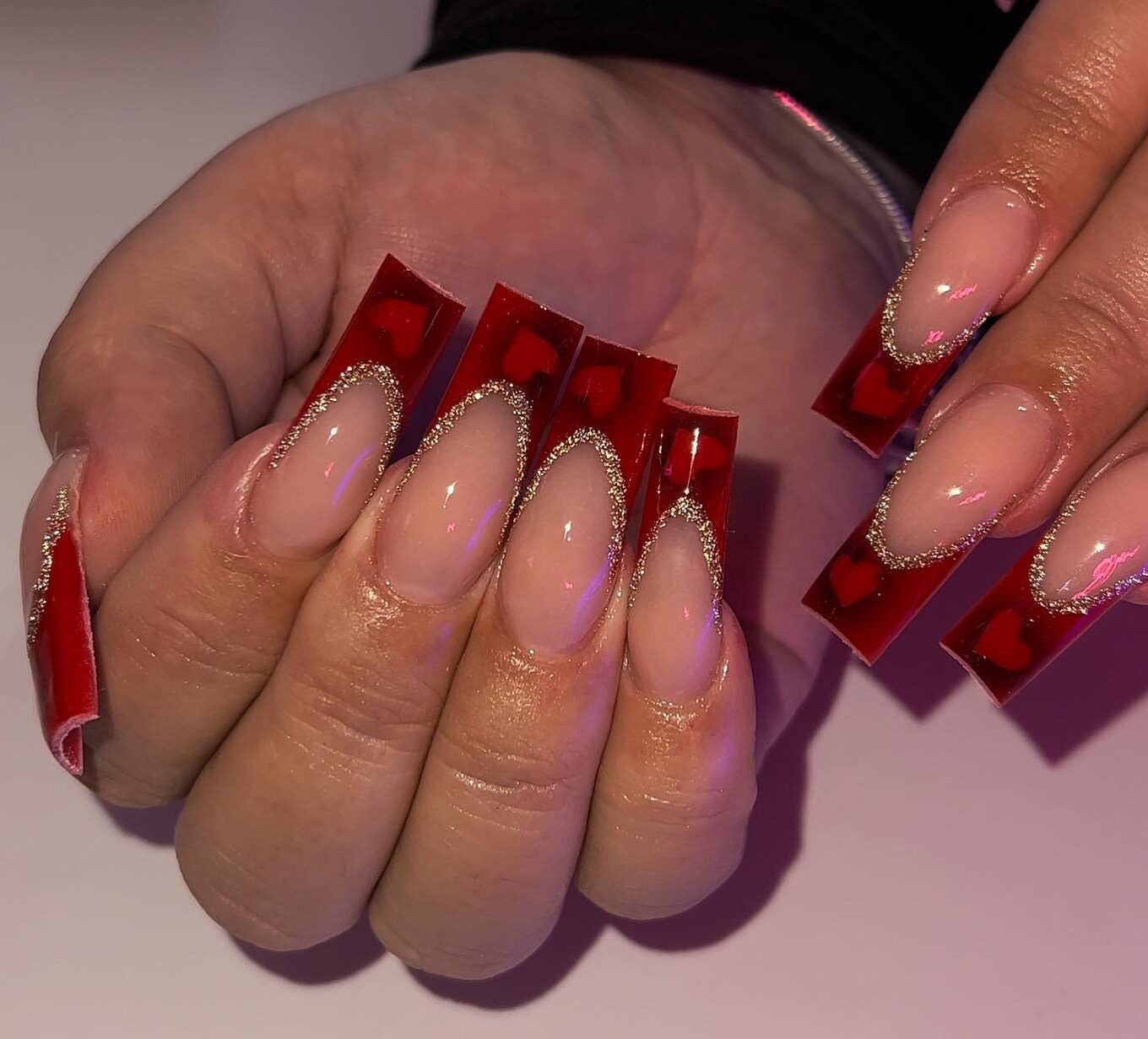 Pointes françaises rouge foncé avec contour pailleté doré et ombres en forme de cœur nail art sur ongles longs carrés