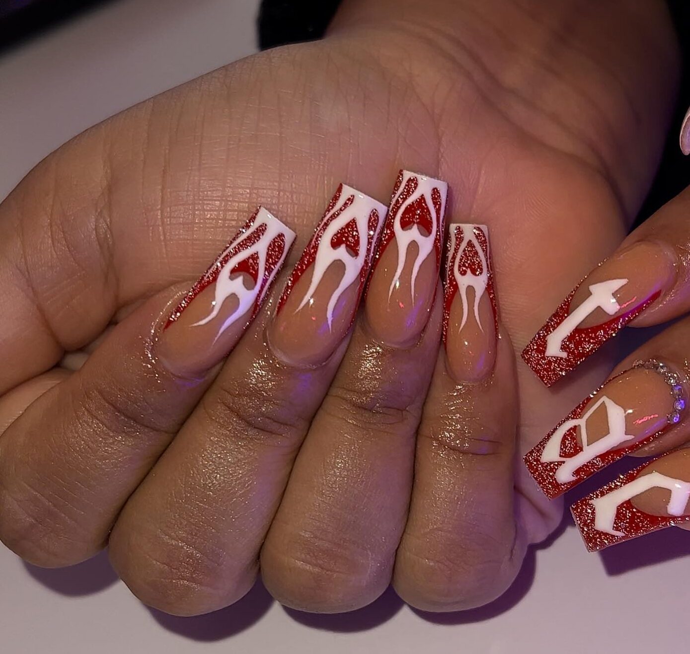 Ongles en acrylique de forme carrée nude. avec des pointes françaises rouges scintillantes et des flammes de cœur blanc nail art