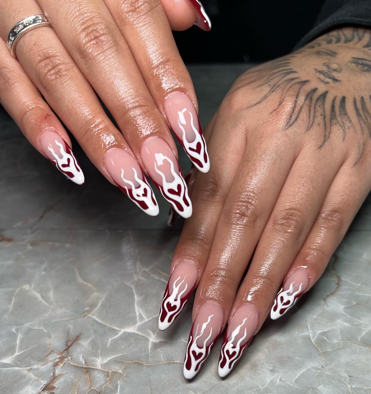 Pointes françaises rouge foncé avec des flammes de cœur blanc nail art sur de longs ongles à talons aiguilles