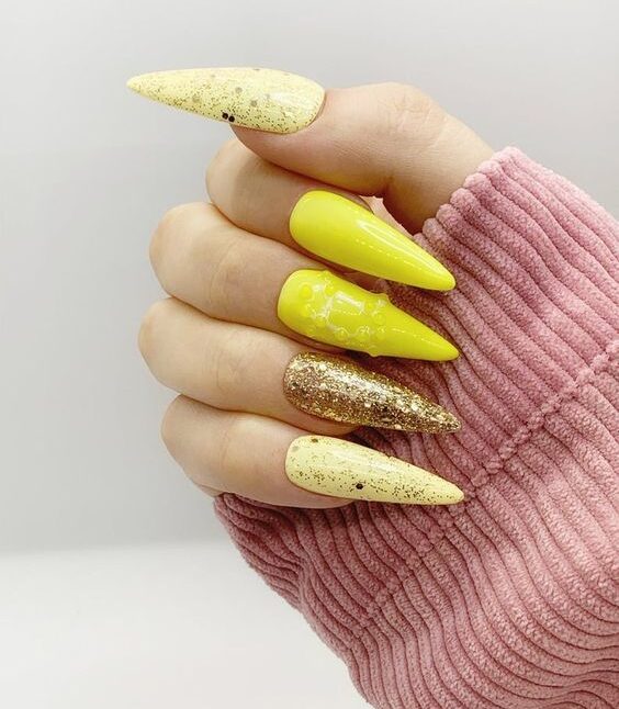 Couleur d’ongle jaune avec des paillettes dorées sur de longs ongles d’extension en forme de talon aiguille