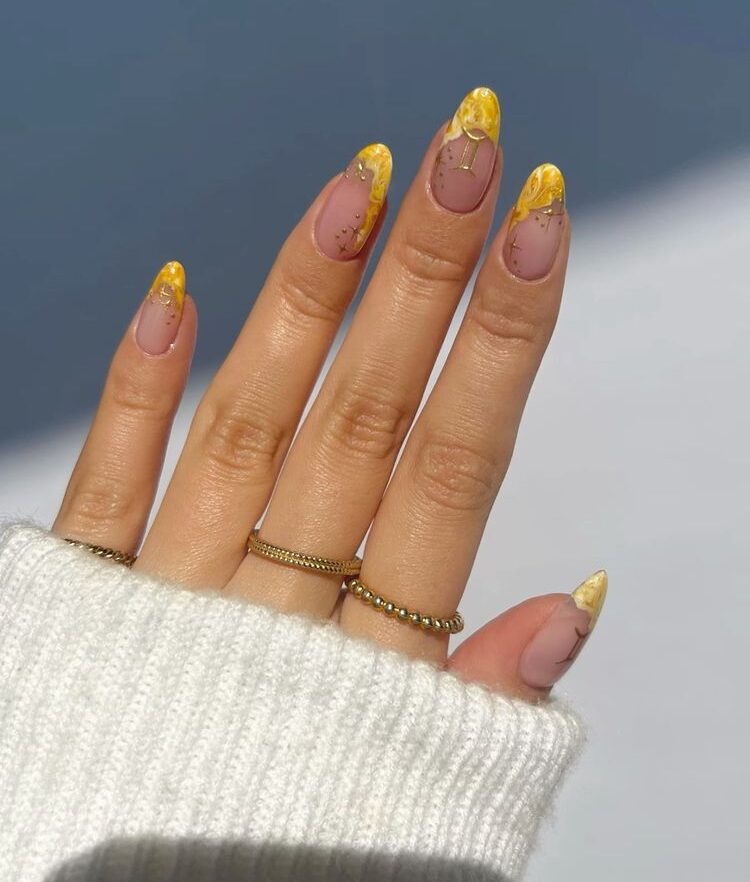 Pointes françaises marbrées jaune vif avec signe Gémeaux doré et éléments célestes nail arts sur ongles ronds moyens