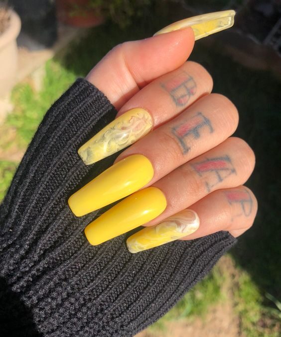 Vernis à ongles jaune et nail art en marbre jaune sur de longs ongles en acrylique en forme de cercueil